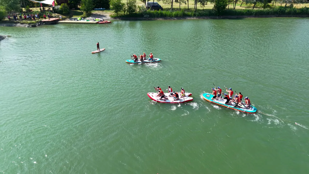 Vista dall'alto di tre equipaggi che pagaiano in sincrono su SUP da squadra